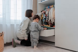 a woman and a child are looking at clothes in a closet