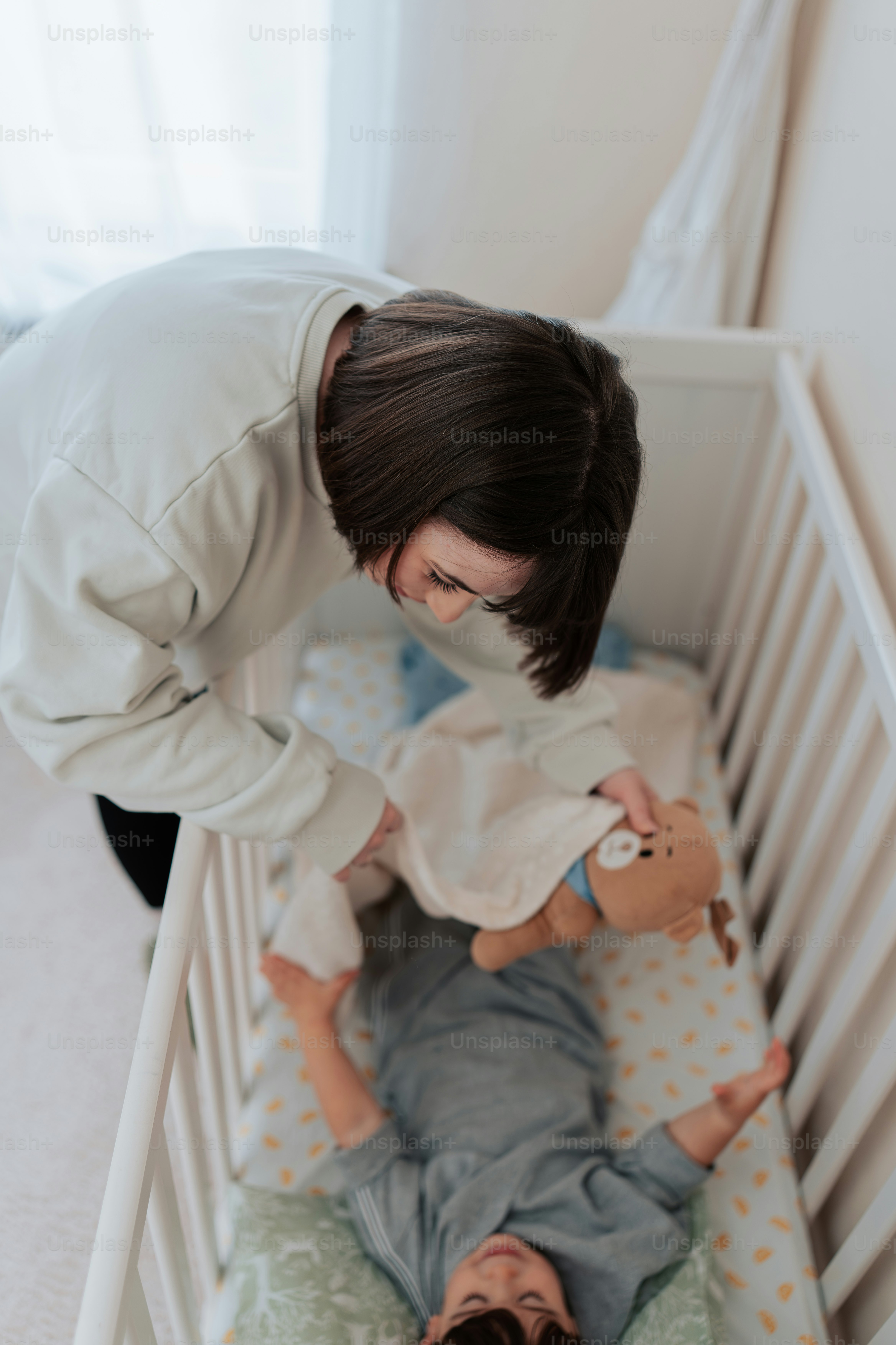 a woman standing over a baby in a crib