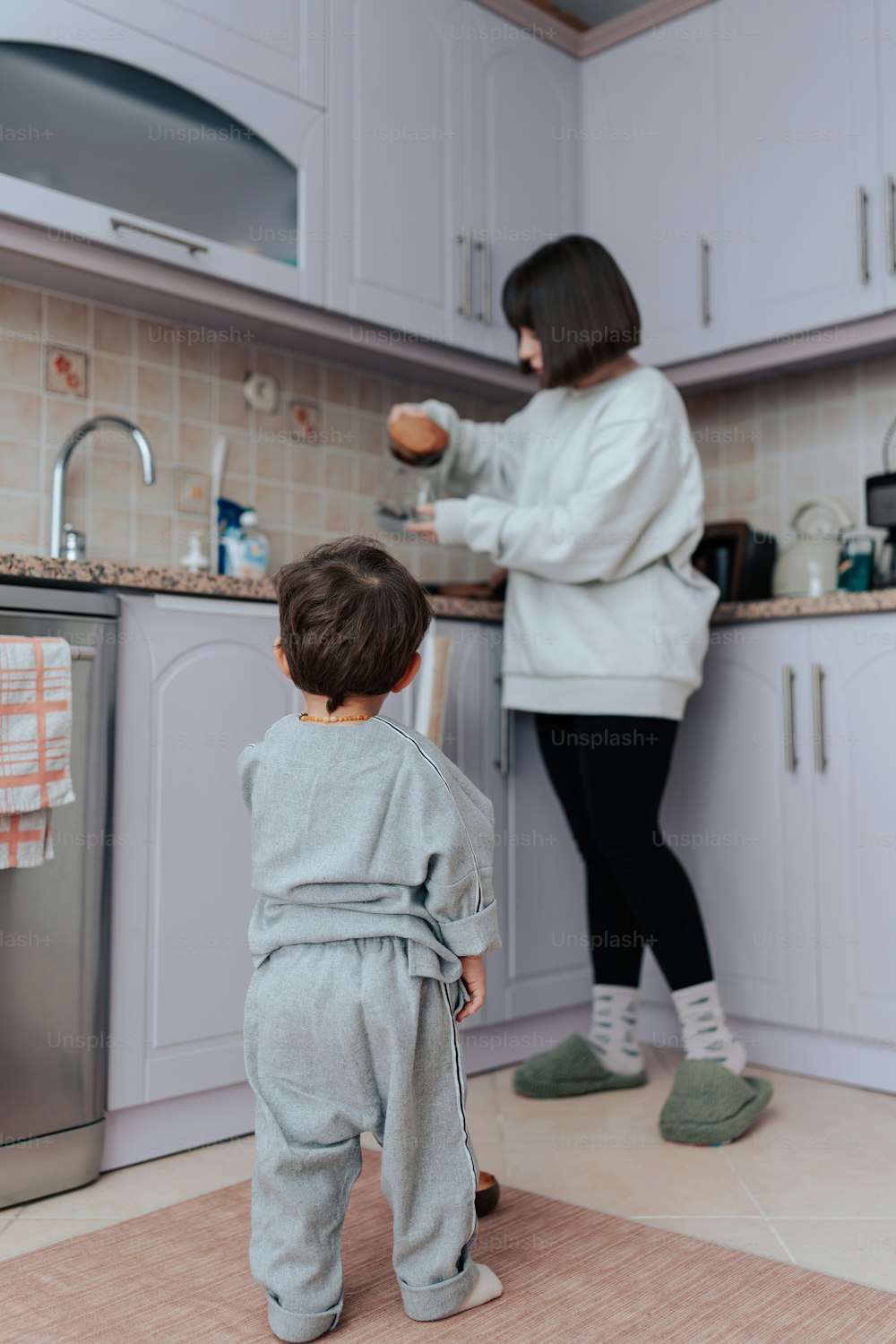 a little boy standing in a kitchen next to a woman