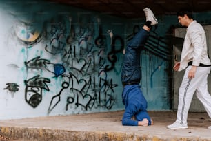a man is doing a handstand in front of a graffiti covered wall