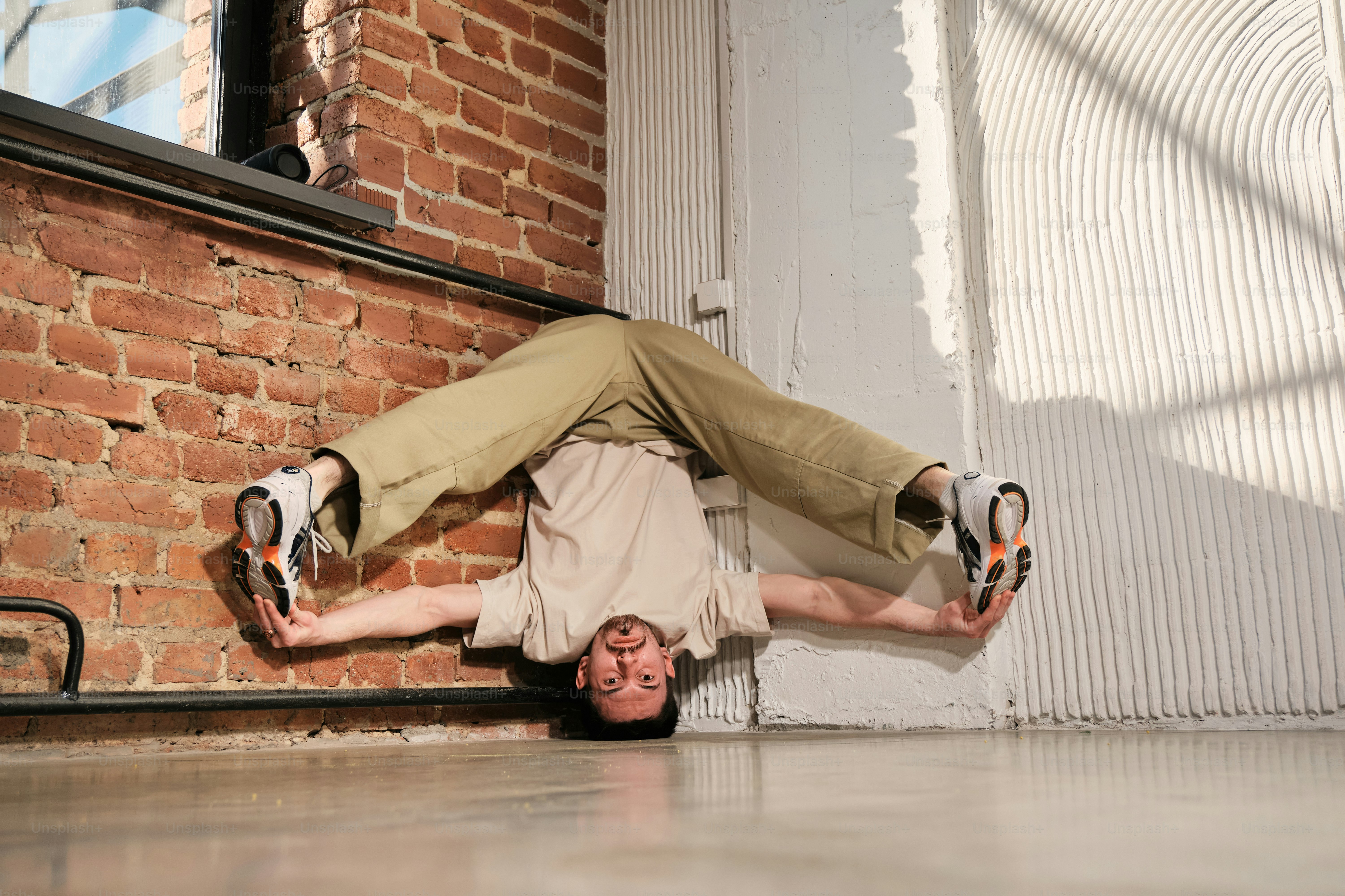 Ein Mann macht einen Handstand vor einer Ziegelmauer