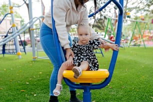 a woman helping a toddler play on a swing set