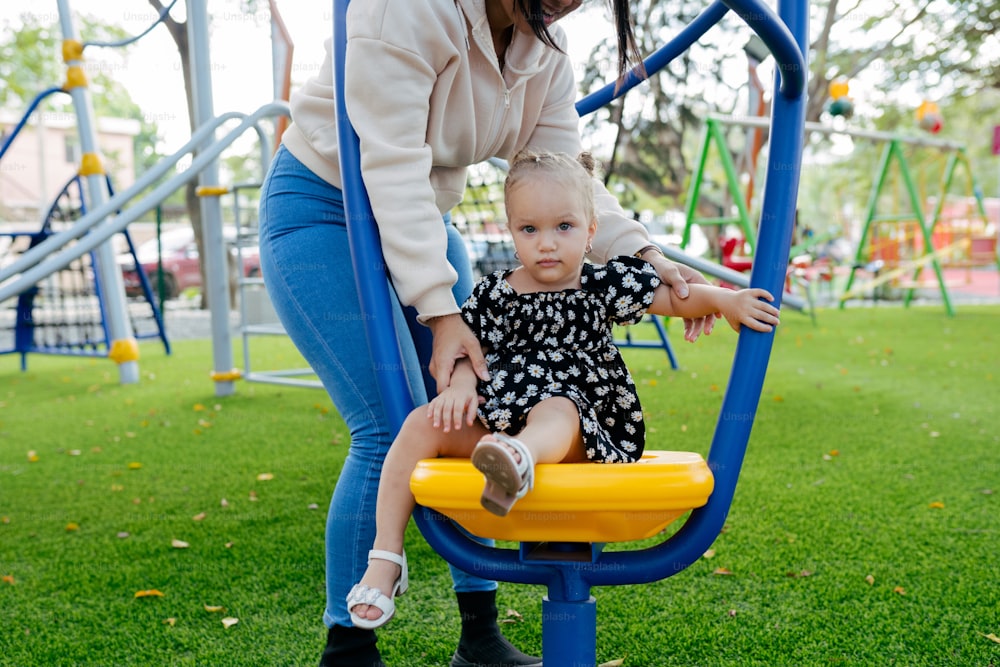 a woman helping a toddler play on a swing set