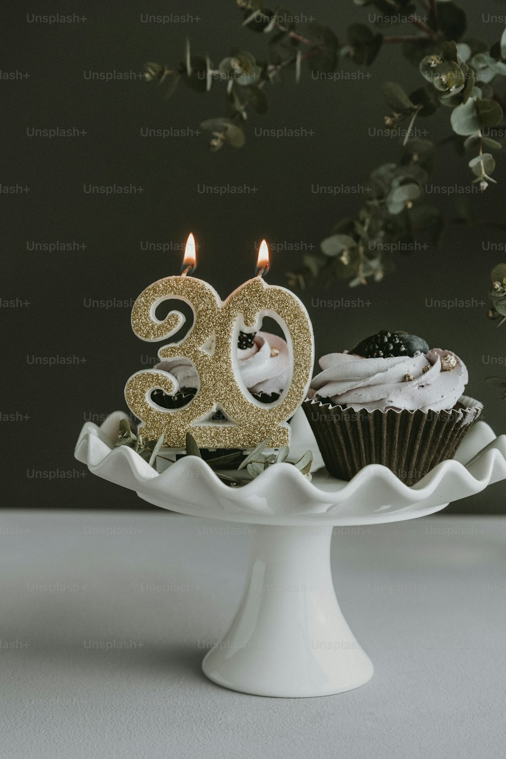컵케이크와 촛불을 얹은 흰색 케이크 접시