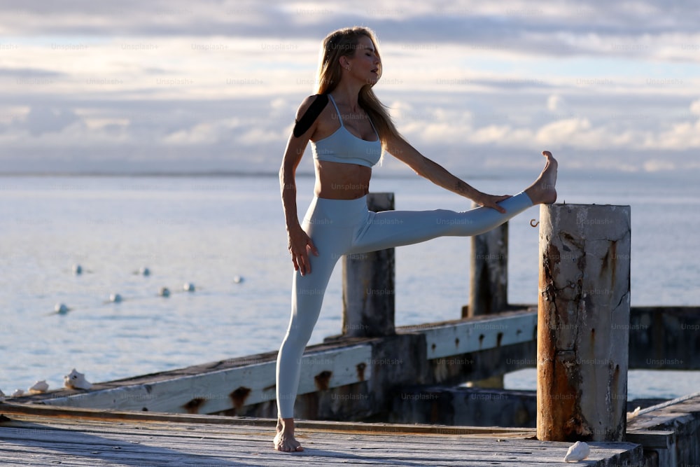 a woman in a white sports bra top and leggings stands on a dock