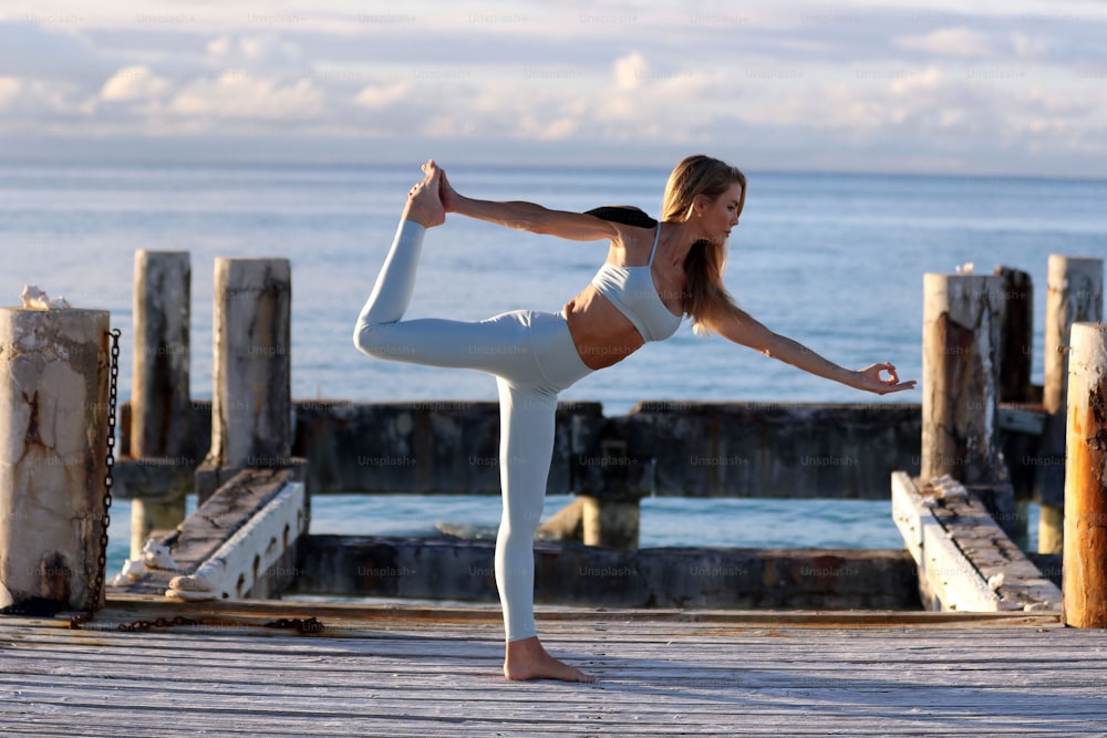 eine Frau, die eine Yoga-Pose auf einem Dock macht