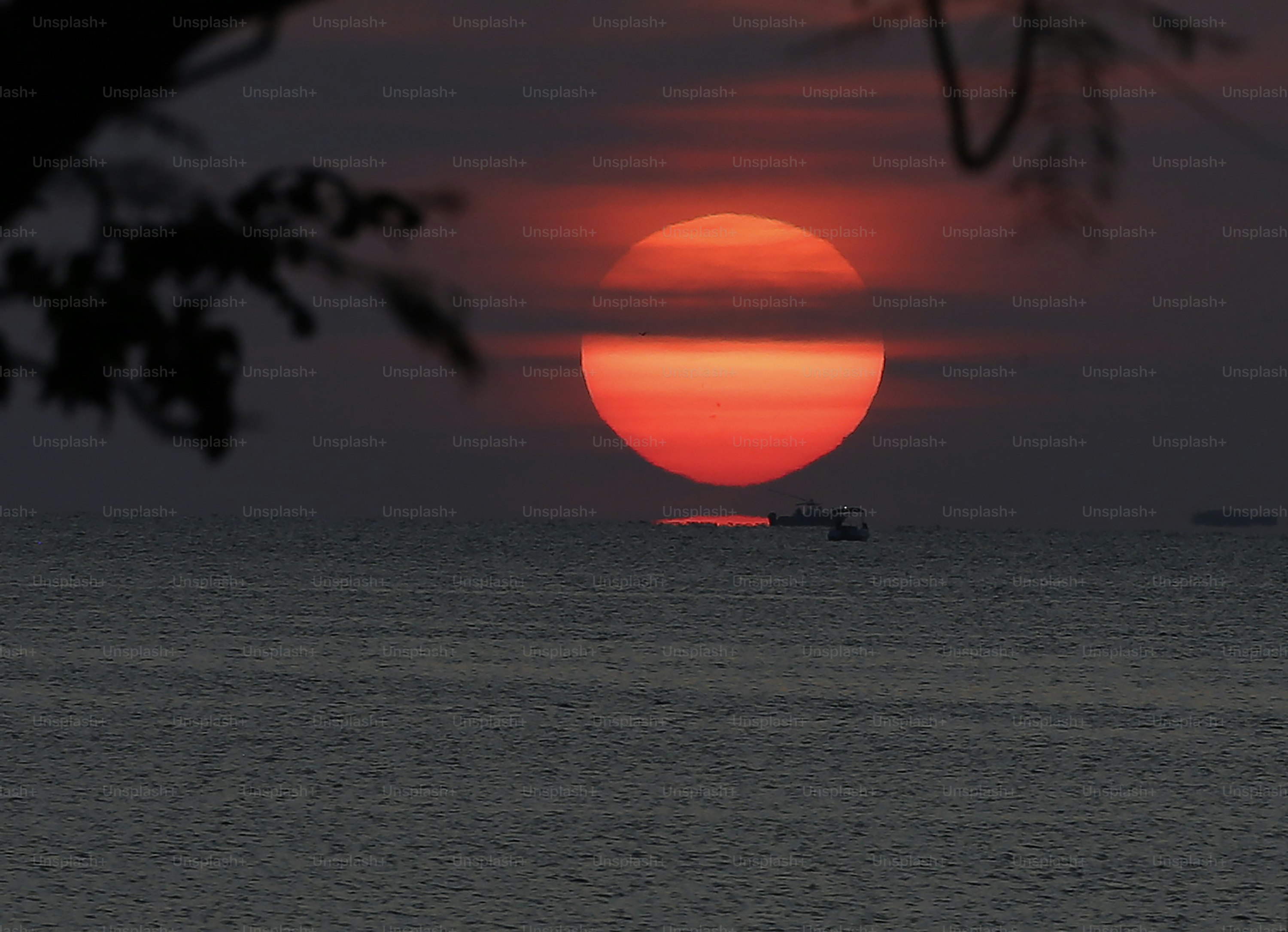 Die Sonne geht über dem Meer unter, mit einem Boot in der Ferne