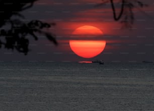 the sun is setting over the ocean with a boat in the distance