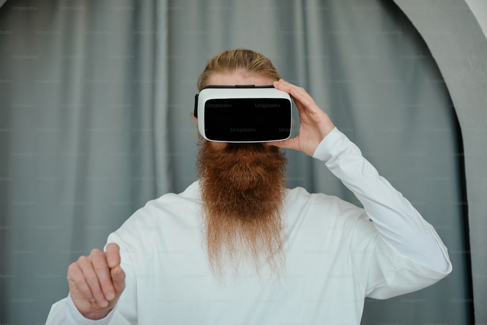 a man with a long beard is holding a virtual device up to his face