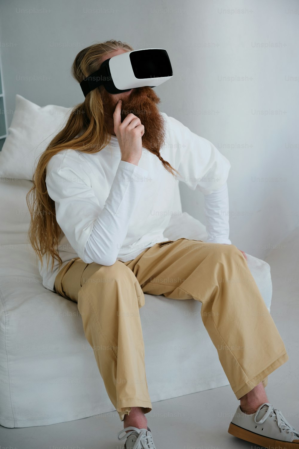 a woman sitting on a couch wearing a white shirt and tan pants