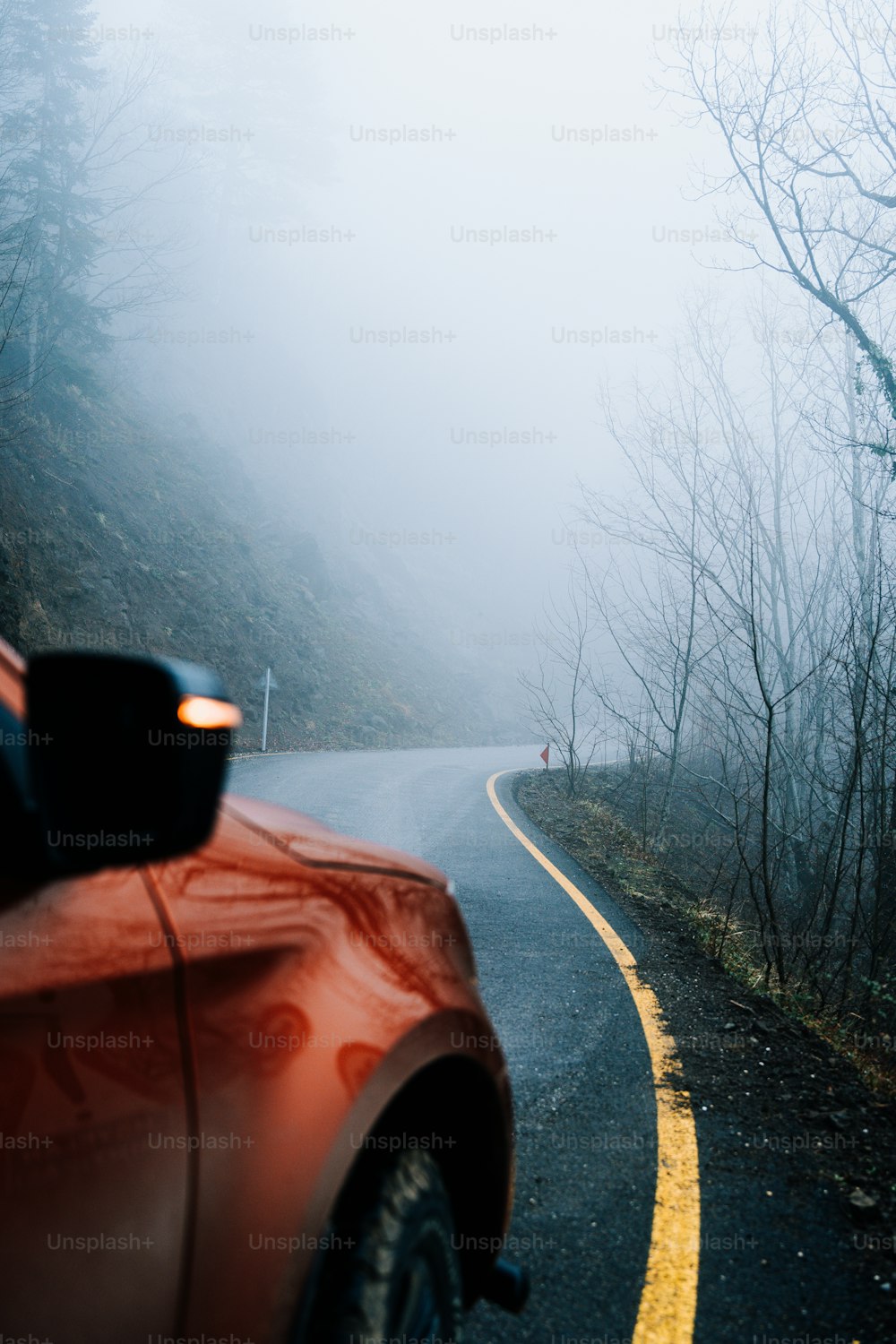 a red car driving down a foggy road