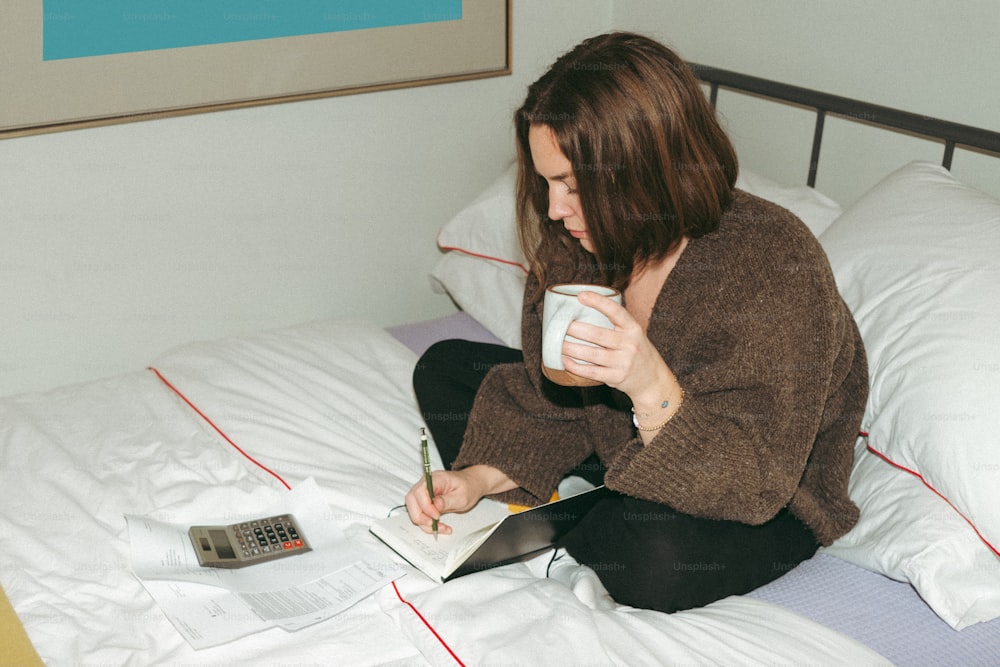 uma mulher sentada em uma cama segurando uma xícara de café