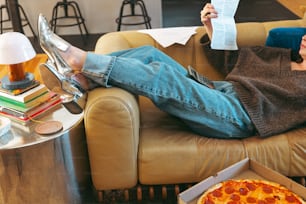 eine Frau, die auf einer Couch sitzt, eine Zeitung liest und eine Pizza isst