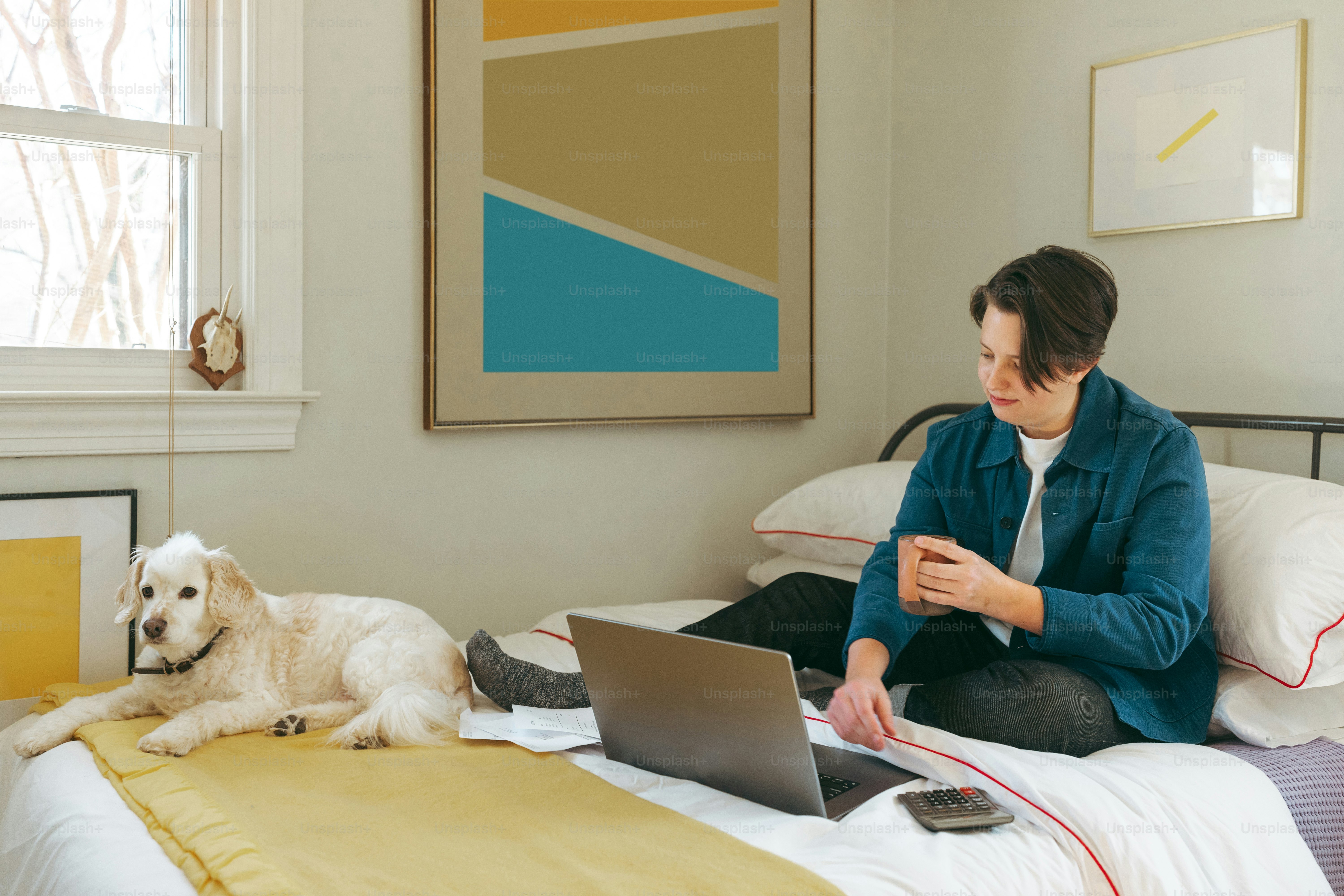 a woman sitting on a bed with a laptop and a dog