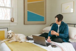 una mujer sentada en una cama con una computadora portátil y un perro