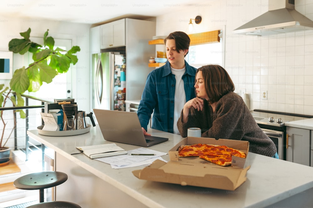 a man and a woman standing in a kitchen with a pizza box on the counter