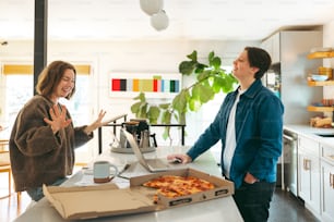 a couple of women standing in a kitchen next to a box of pizza