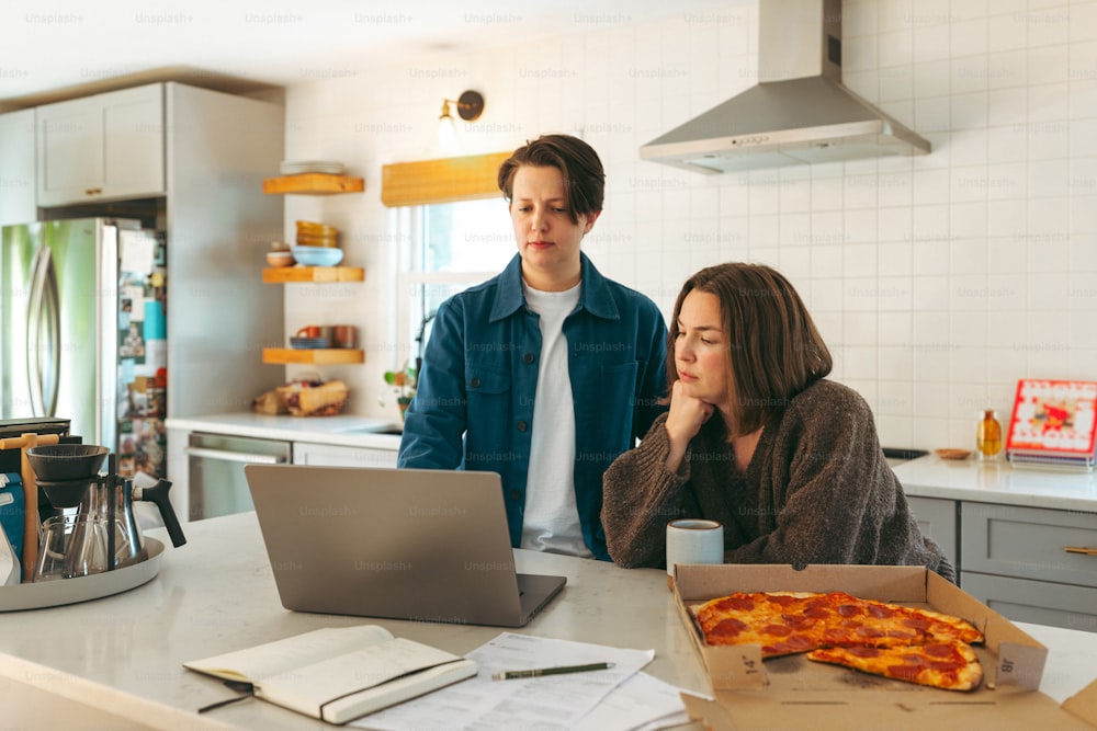 um homem e uma mulher em pé em uma cozinha olhando para um laptop
