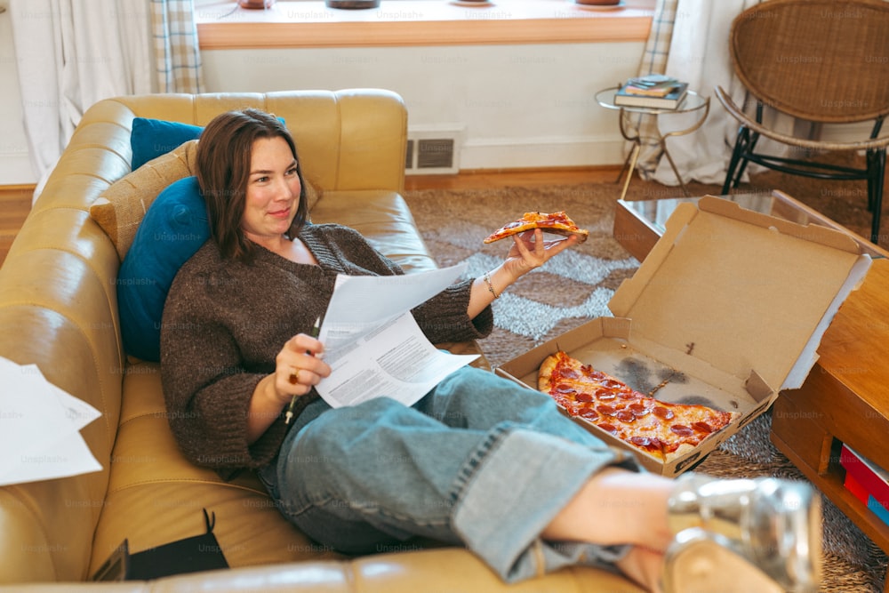 eine Frau, die auf einer Couch sitzt und ein Stück Pizza isst