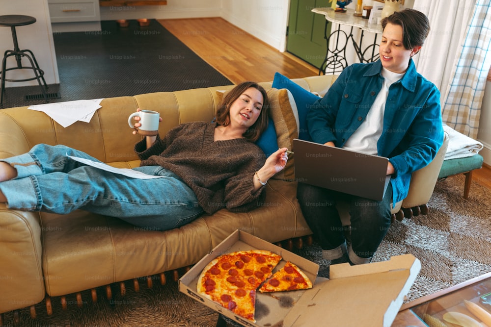a man and woman sitting on a couch with pizza and a laptop