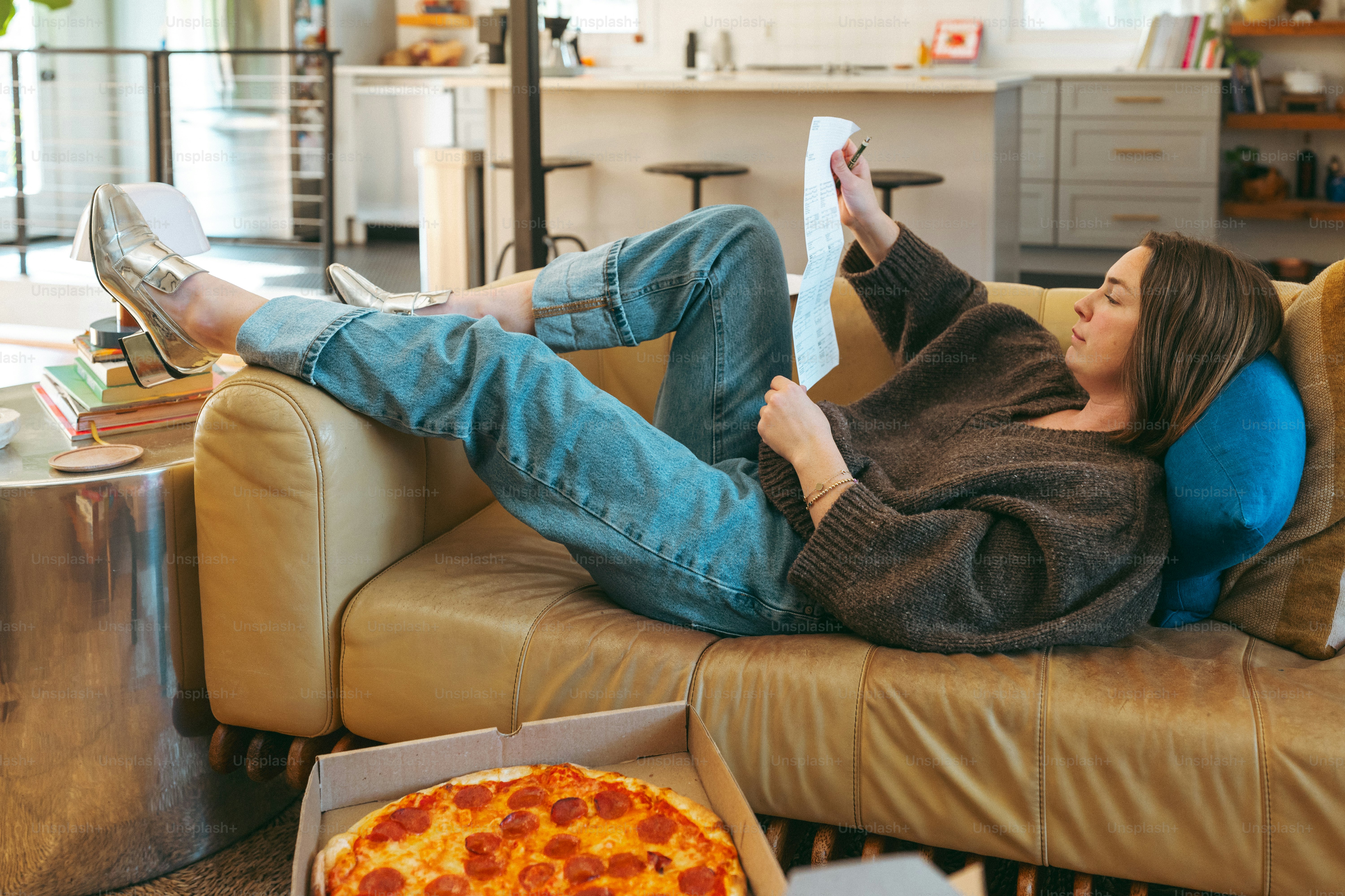 uma mulher sentada em um sofá com uma pizza à sua frente