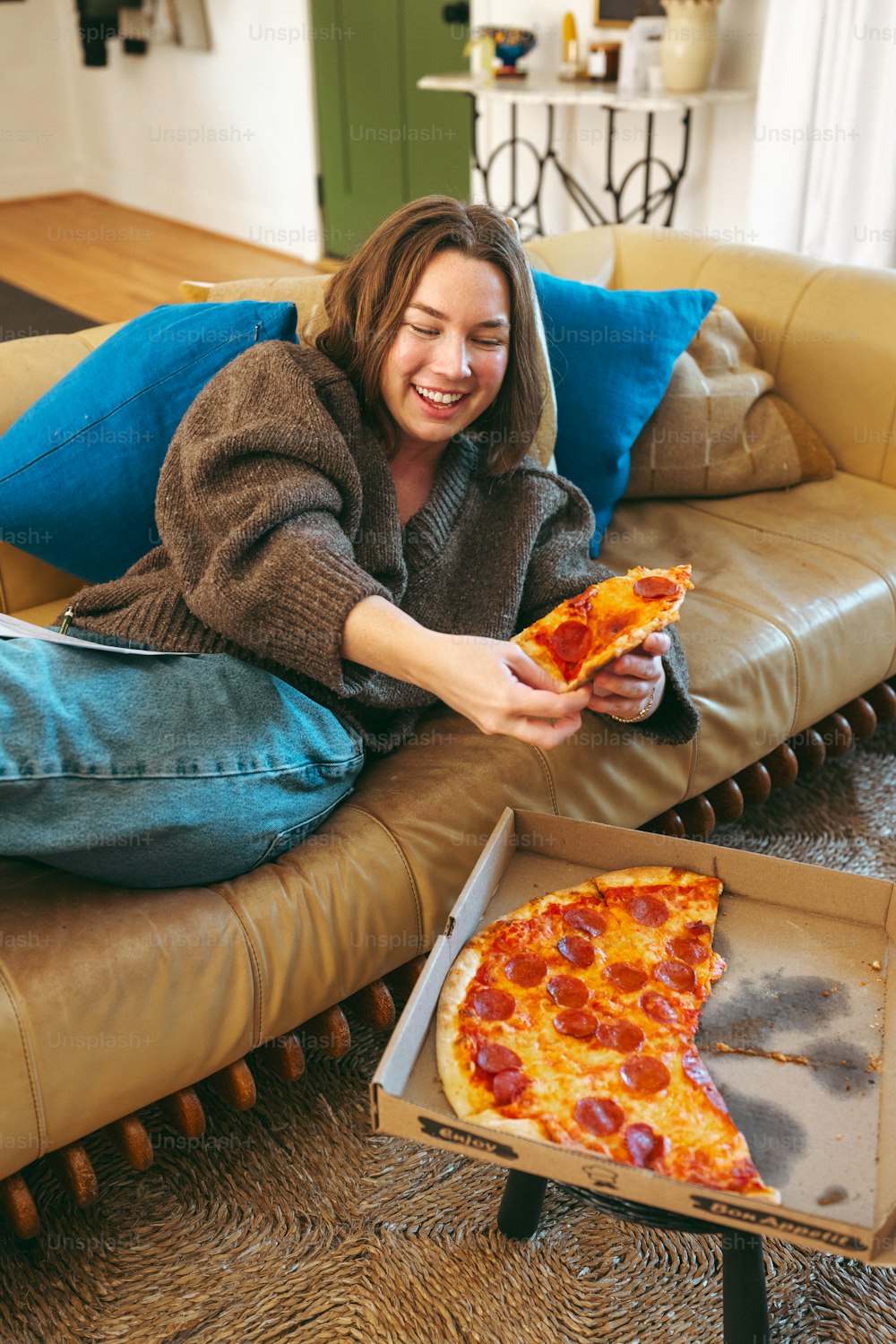 a woman sitting on a couch holding a slice of pizza