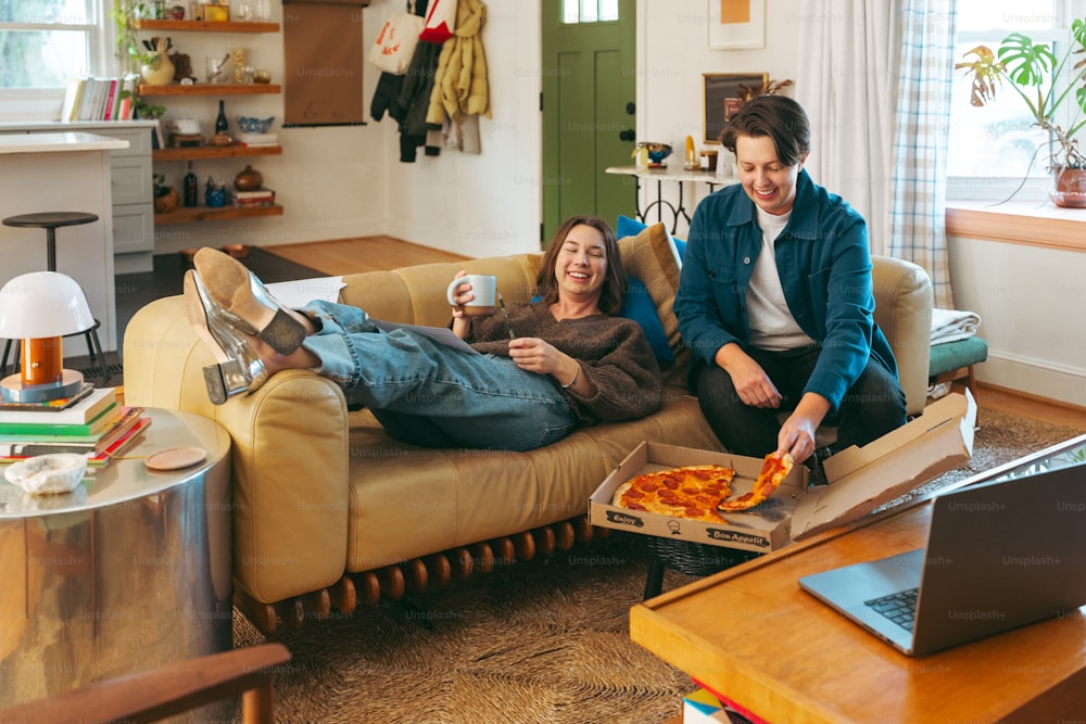 a man and woman sitting on a couch eating pizza