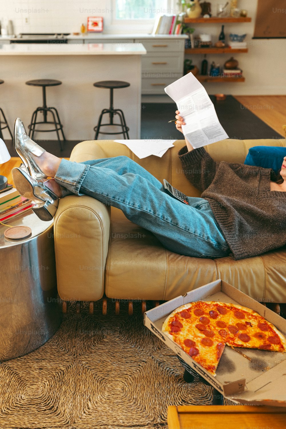 eine Person, die auf einer Couch sitzt, ein Buch liest und Pizza isst