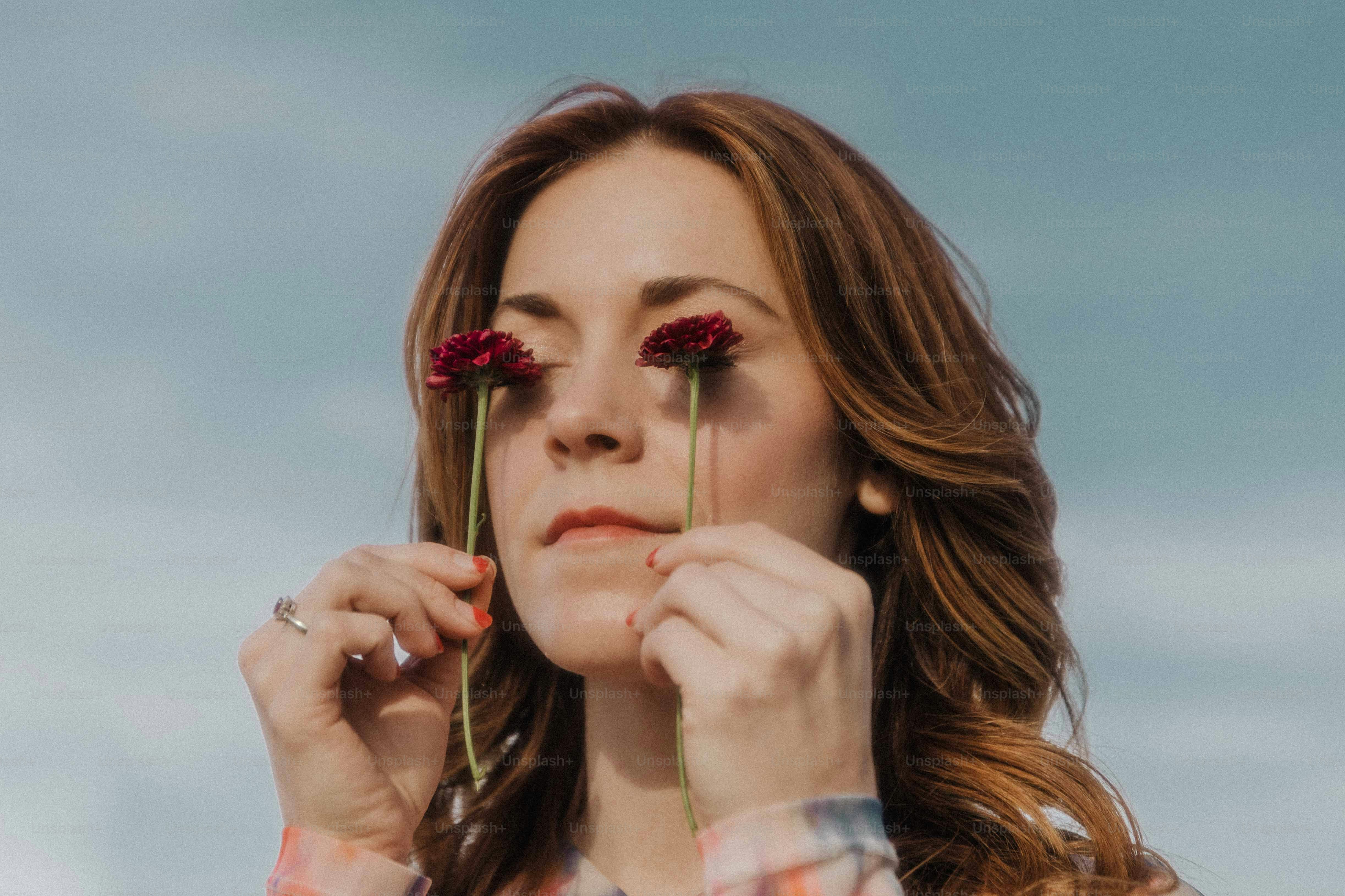 a woman holding two red flowers to her face