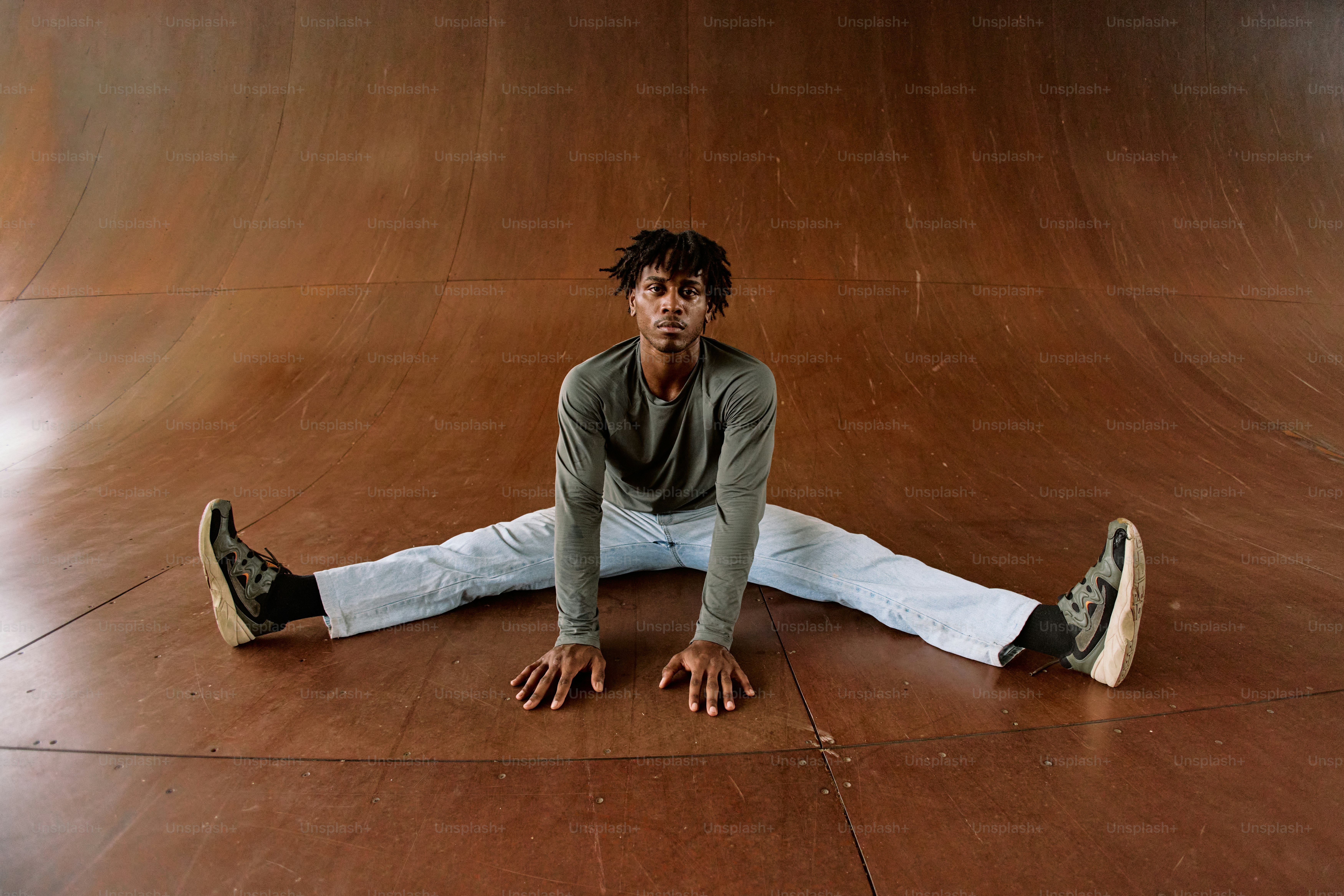 Ein Mann sitzt auf dem Boden vor einer Skateboard-Rampe