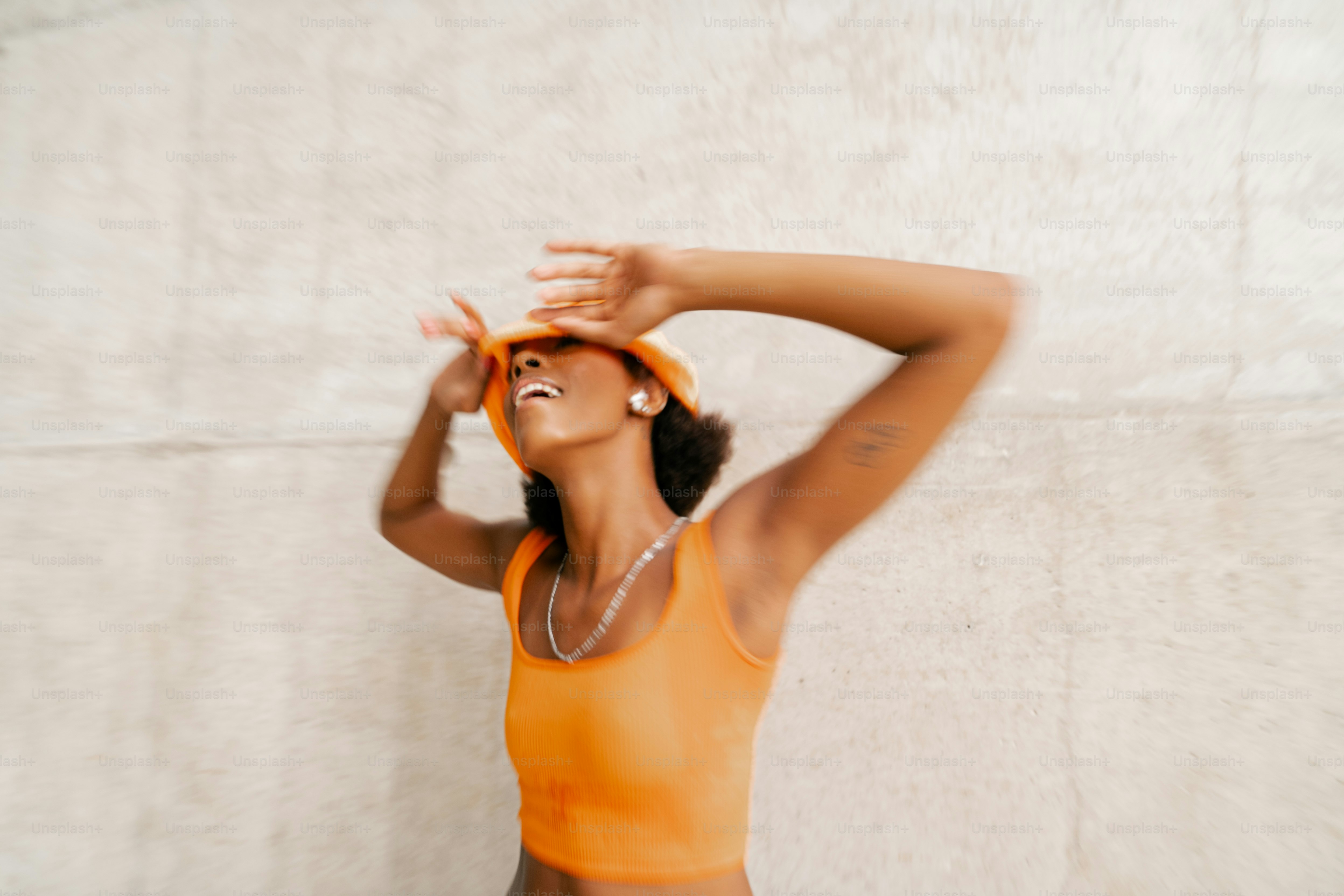 A woman in an orange tank top is holding her hands behind her head ...