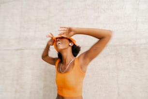 a woman in an orange tank top is holding her hands behind her head