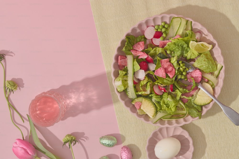 Un plato rosa con una ensalada y unas flores