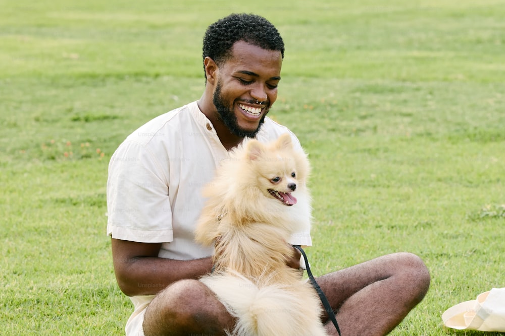 um homem sentado na grama segurando um cachorro pequeno