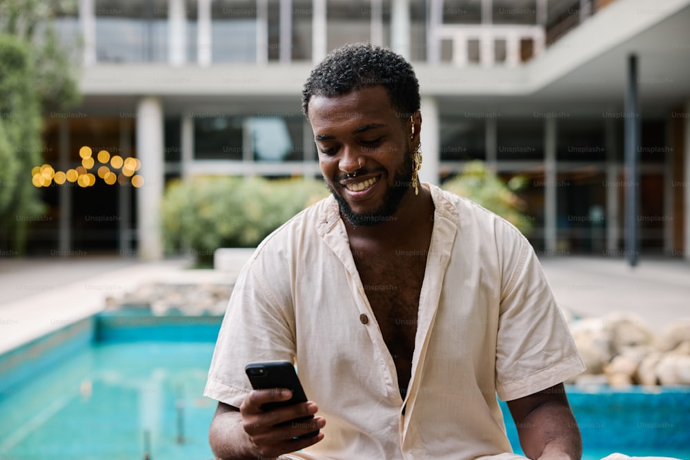 Un hombre sentado frente a una piscina mirando su teléfono celular