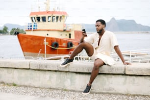 ein Mann sitzt mit einem Handy auf einer Mauer