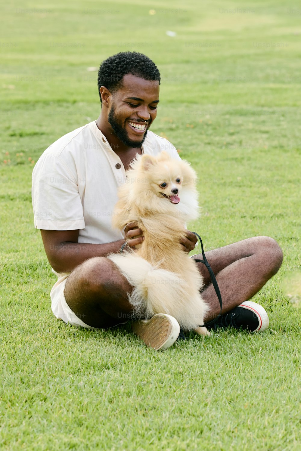 芝生に座り、小型犬を抱いた男性