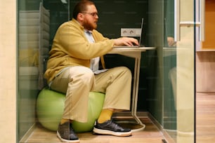 a man sitting on a ball using a laptop
