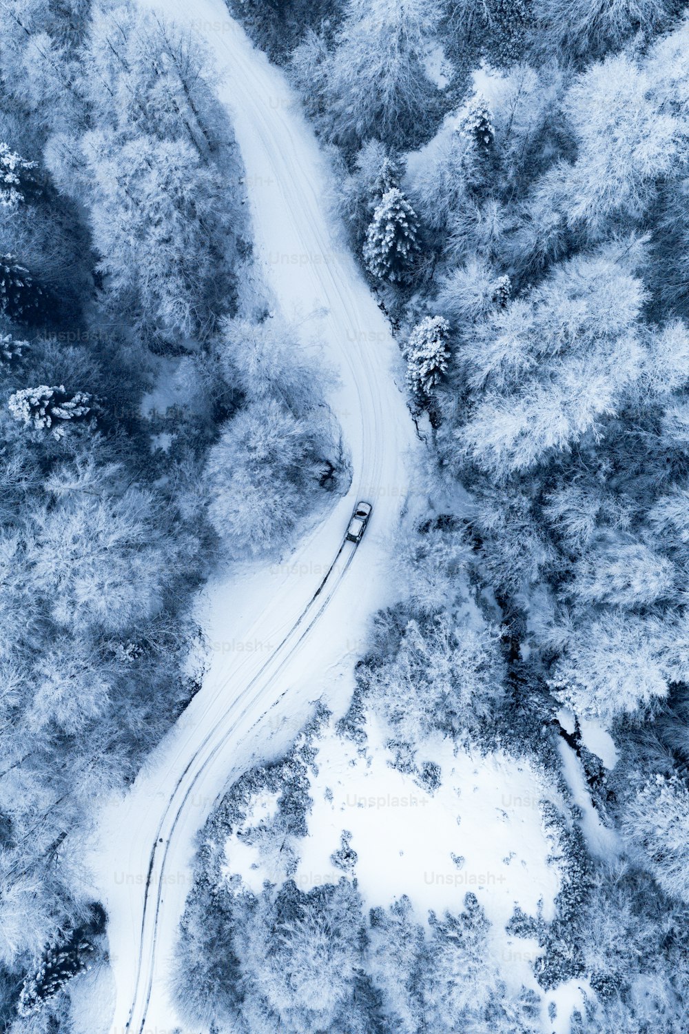 an aerial view of a car driving down a snowy road