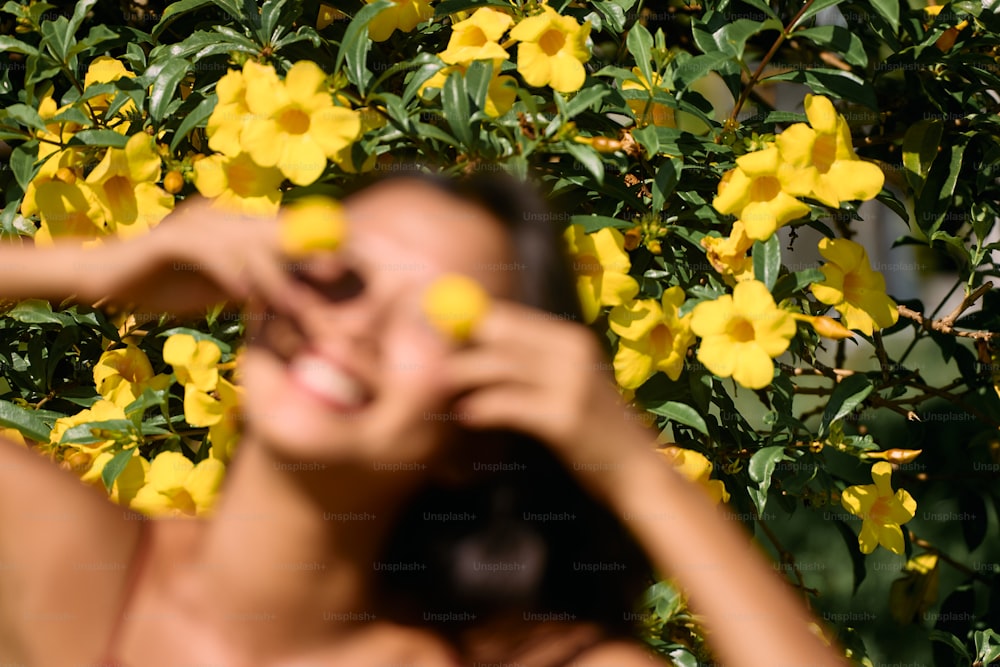 a woman standing in front of a bush with yellow flowers