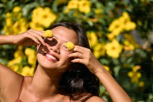 una mujer sosteniendo dos flores amarillas frente a su cara