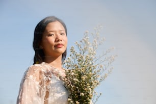 eine Frau in einem weißen Kleid mit einem Blumenstrauß in der Hand