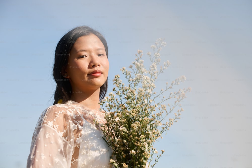 una donna in un vestito bianco che tiene un mazzo di fiori