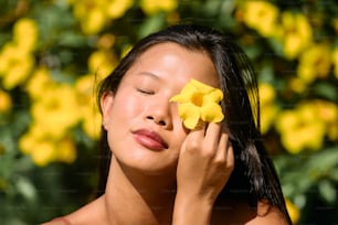 una mujer sosteniendo una flor amarilla en su cara