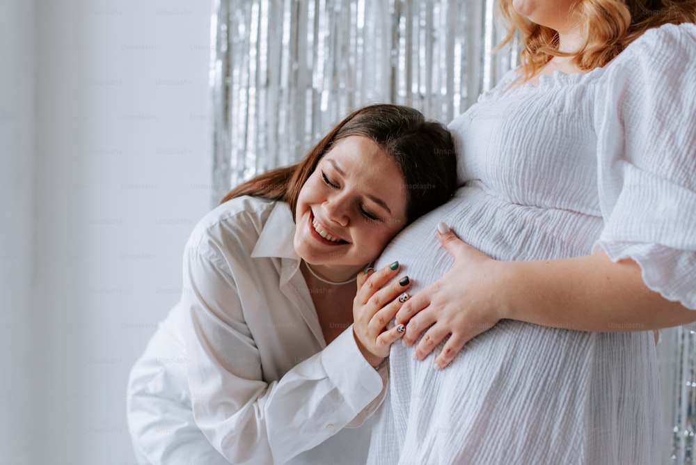a woman is hugging a pregnant woman in a white dress