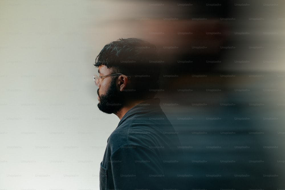 a man with glasses and a beard standing in front of a white wall