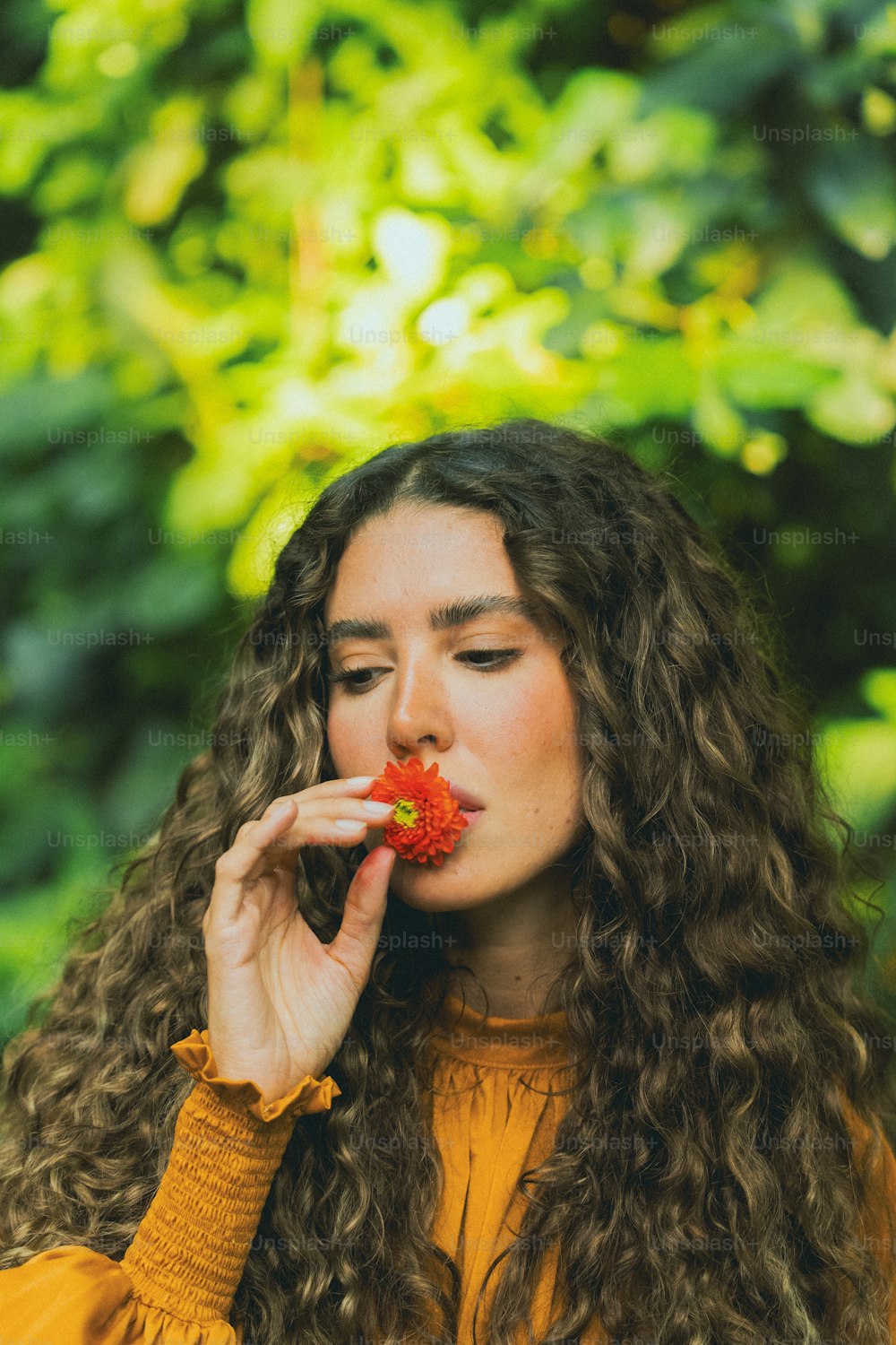 a woman with long curly hair holding a flower in her mouth