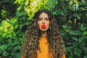 a woman with long curly hair and a red flower in her mouth