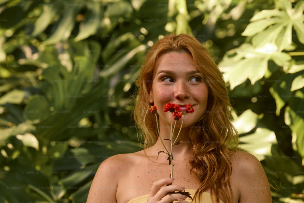 una mujer sosteniendo una flor roja frente a su cara