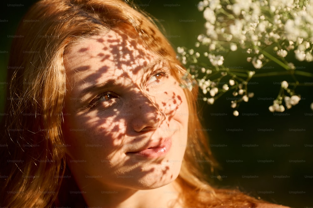 a woman with freckles on her face and a bush of flowers behind her